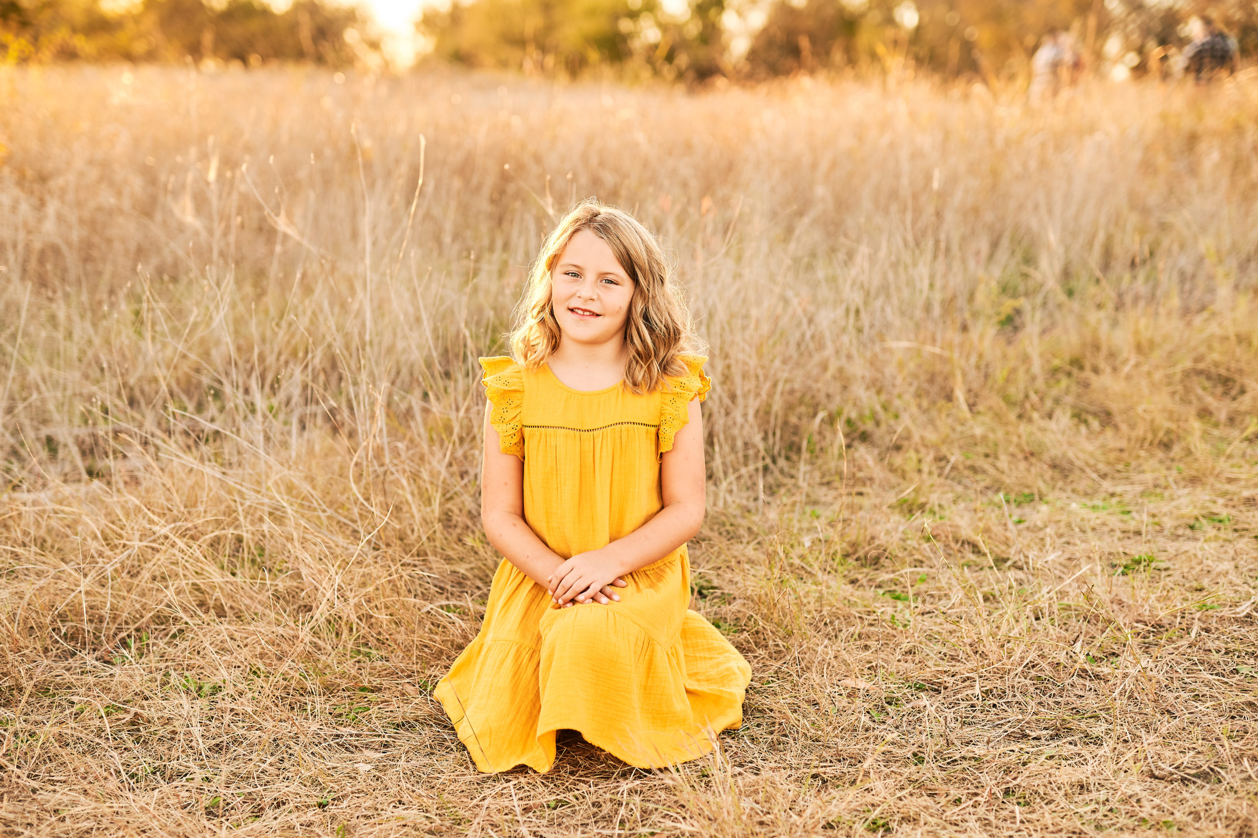 Young girl in a yellow dress sitting down in the grass during golden hour