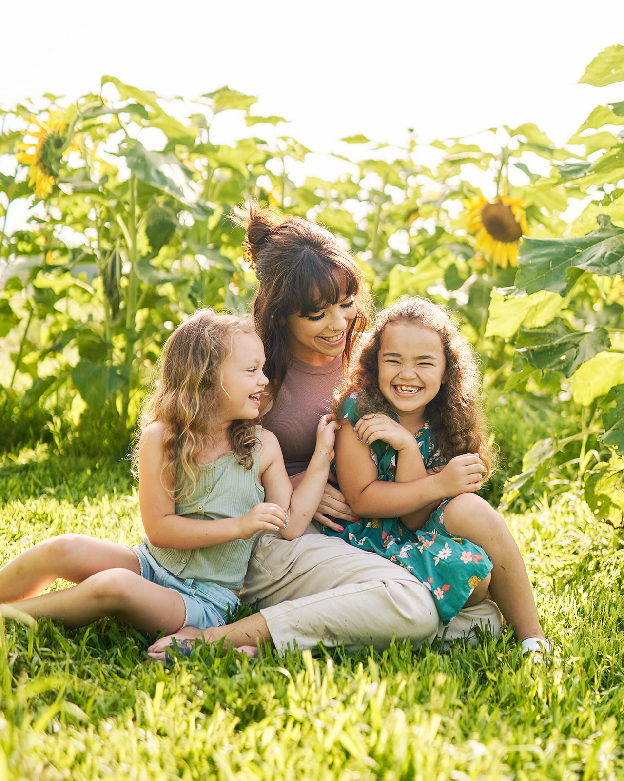 Mother and her two daughters having a tickle fight in a sunflower field.